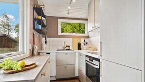 Cuina moderna amb armaris blancs, forn integrat i finestra amb vista a vegetació.