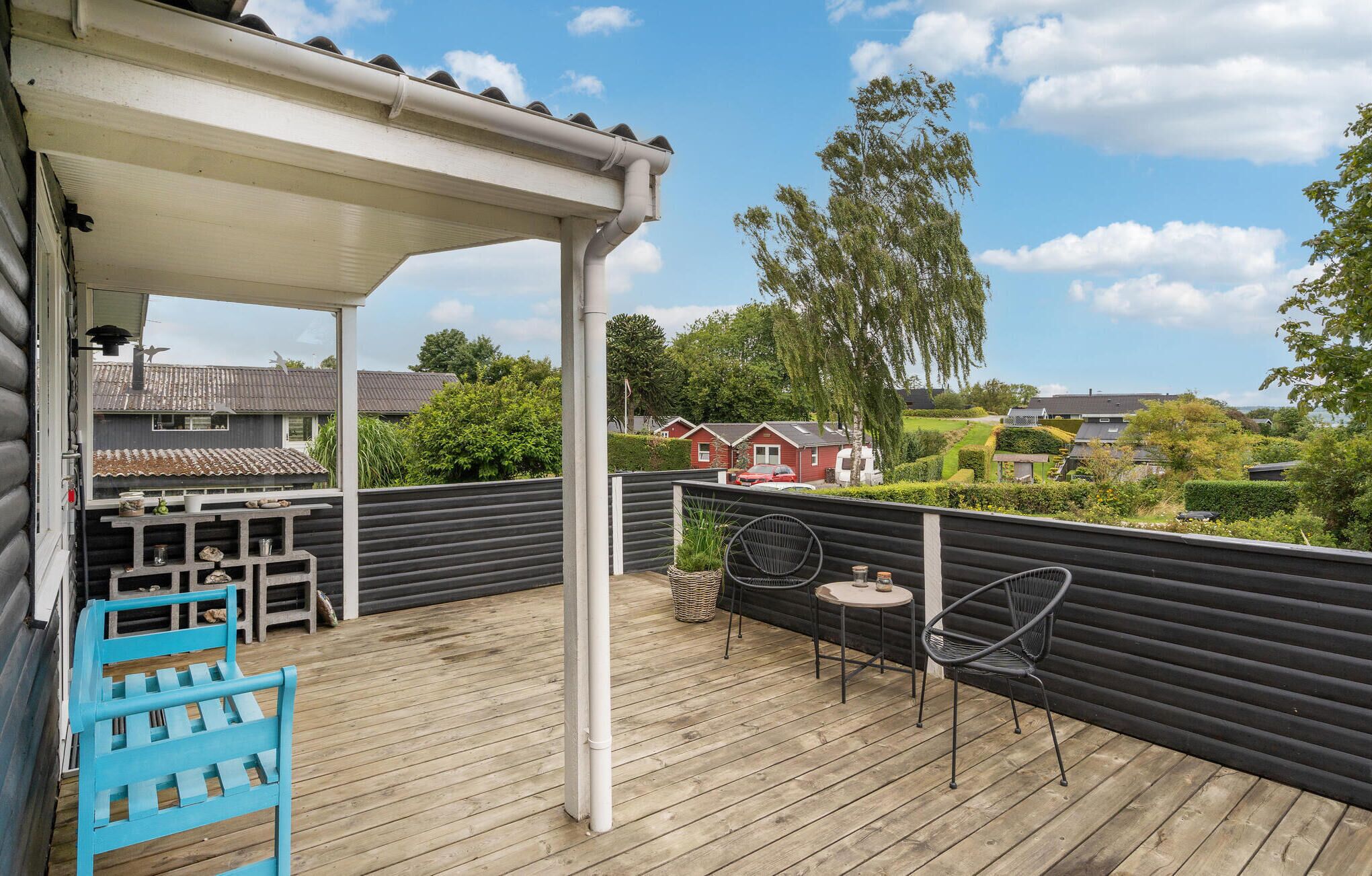 Eine Holzterrasse mit überdachter Sitzecke, einem blauen Stuhl und einem Tisch.