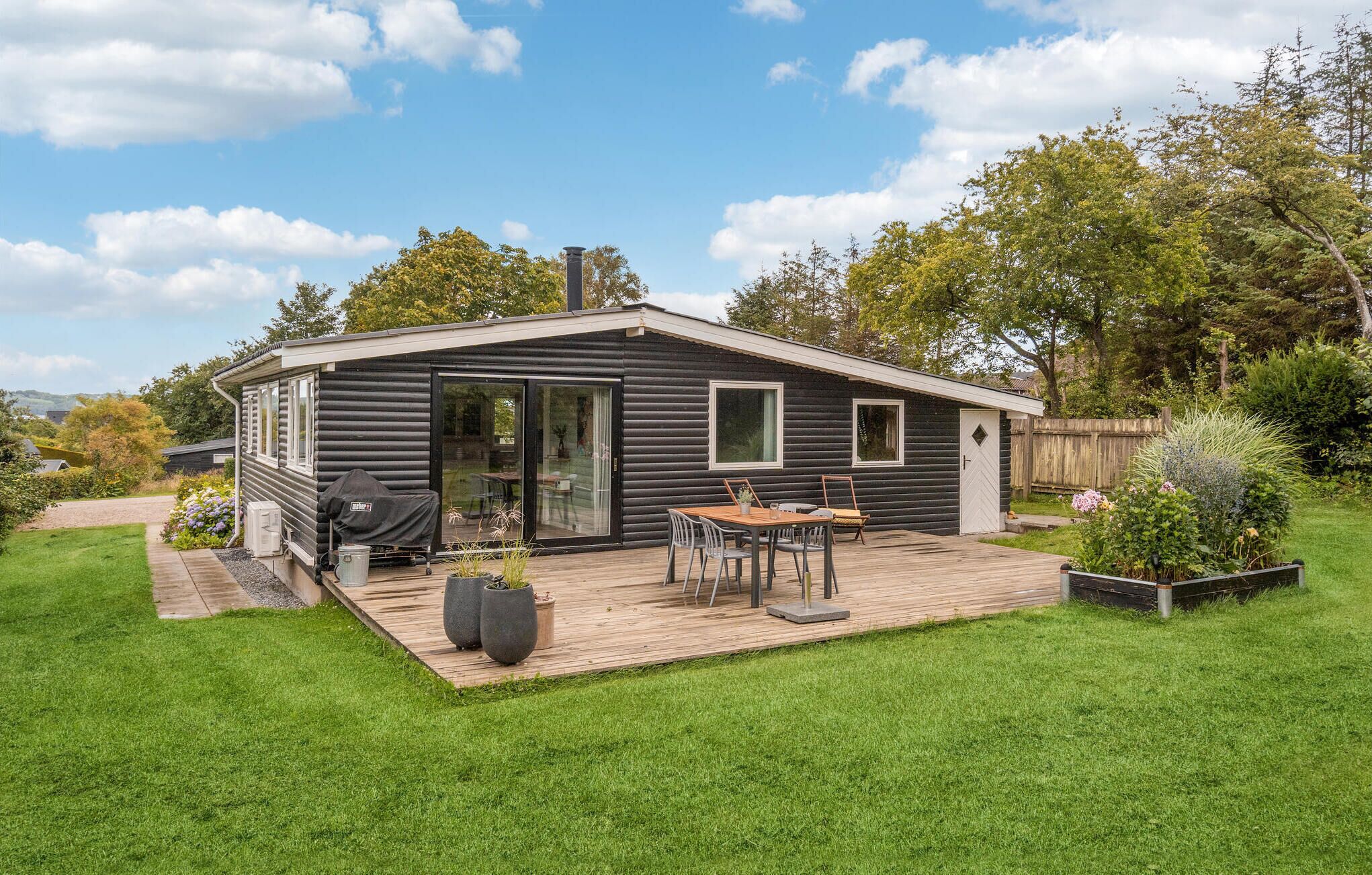 A modern log cabin with a patio, outdoor seating, and a large sliding glass door.