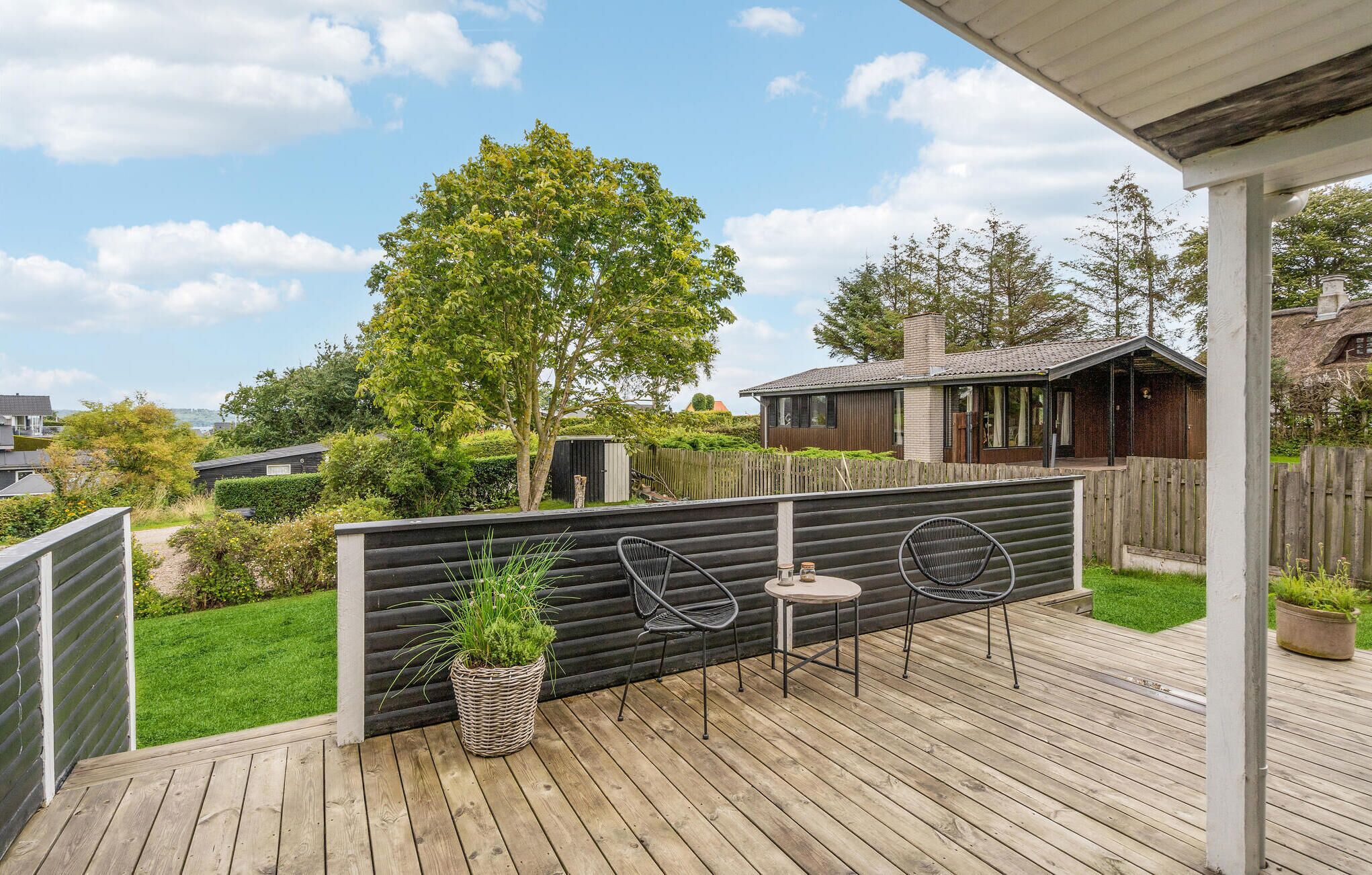 Eine Holzterrasse mit Tisch und Stühlen, umgeben von einem Holzzaun und einem großen Baum.