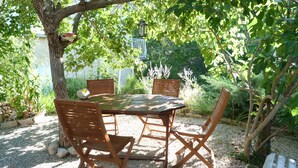 Un espacio al aire libre para comer con una mesa y sillas de madera, rodeado de grava y follaje.