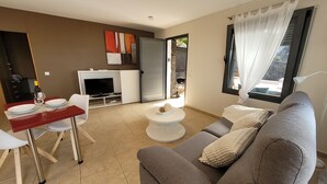 Ein modernes Wohnzimmer mit einem grauen Sofa, einem kleinen weißen Tisch und einem roten Esstisch mit Stühlen.