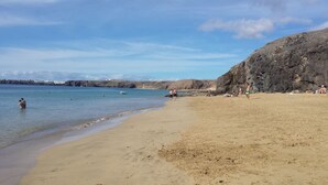 Ein Strand mit klarem Wasser, einer felsigen Klippe und einigen Personen.