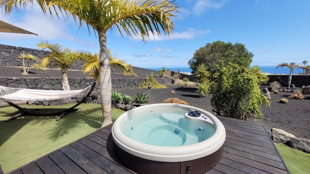 Eine Holzterrasse mit Whirlpool, Hängematte und tropischen Pflanzen.