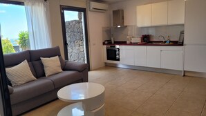 Ein modernes Wohnzimmer mit einem grauen Sofa, einem weißen Couchtisch und einer Küchenzeile mit weißen Schränken und einer roten Arbeitsplatte.