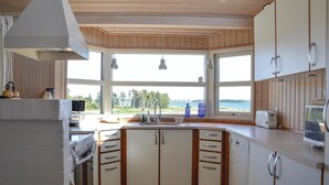 Cocina compacta con armarios de madera, horno integrado y vistas a la playa a través de amplias ventanas.
