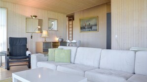 Una sala de estar con un sofá blanco, una silla, una mesa, una lámpara, un radio, una escalera y un cuadro en la pared.