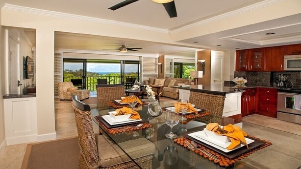 A spacious dining area with a glass table set for four, surrounded by wicker chairs. - The Golden Lotus ~ Pool ~ Jacuzzi ~ Grills ~ (Princeville)