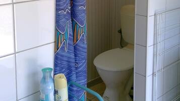 A bathroom with a shower curtain featuring fish patterns, a toilet, and a small table with toiletry bottles.