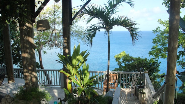 Um deck de madeira com plantas em vasos, um banco e vista para o oceano.