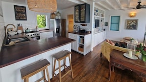 Uma cozinha moderna com ilha central, banquetas de madeira, luminária pendente e vista para o exterior.