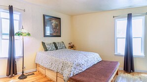 A bedroom with a bed, a bench, a floor lamp, and a painting on the wall.