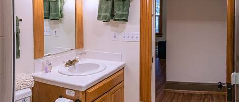 A bathroom with a wooden vanity, a white sink, and a mirror. There are two green towels hanging on the wall.
