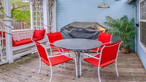 A covered outdoor seating area with a round table and red chairs, a barbecue grill, and a potted plant. - Oak Hideaway Cottage- 1.5 Blocks to OSF (Ashland)