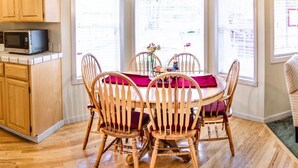 A dining area with a wooden table and chairs, a microwave on the counter, and large windows with blinds. - Oak Hideaway Cottage- 1.5 Blocks to OSF (Ashland)