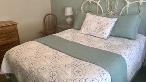 A neatly made bed with a patterned bedspread and pillows, a wooden nightstand with a lamp, and a chair in a bedroom. - Oak Hideaway Cottage- 1.5 Blocks to OSF (Ashland)