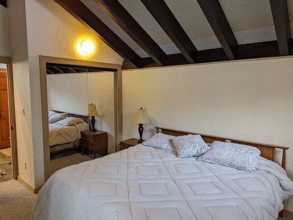 Un dormitorio con una cama grande, una mesita de noche con lámpara, un espejo y techo de madera.