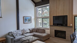 A modern living room with a sectional sofa, a fireplace, a television, and large windows.