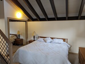 A bedroom with a large bed, wooden headboard, two bedside tables with lamps, a mirror, and a wooden staircase.
