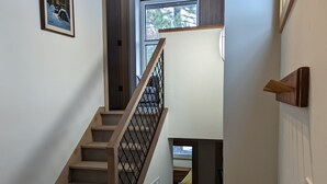 A staircase with wooden steps and a metal railing, leading to a room with a bed and a window.