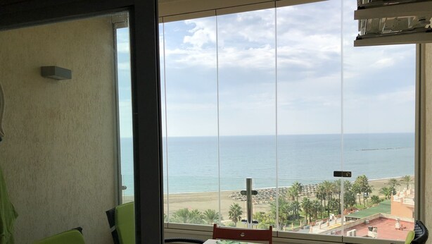 Una stanza con una grande finestra vista spiaggia, un tavolo con un cuscino verde e due sedie.
