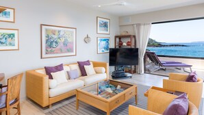 A modern living room with a sofa, coffee table, and lounge chairs. There is a television and artwork on the walls. - Beachfront  / Corner  / Renovated / 2nd floor condo unit: F-204 (Wailea-Makena)