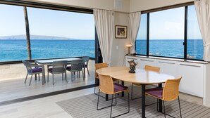 A dining area with a view of the sea, featuring a round table with chairs, a patterned rug, and a window with curtains. - Beachfront  / Corner  / Renovated / 2nd floor condo unit: F-204 (Wailea-Makena)