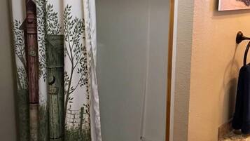 A shower area with a glass door and a curtain featuring a forest scene.