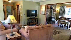 A cozy living room with a brown sofa, a television, a lamp, and a fireplace.