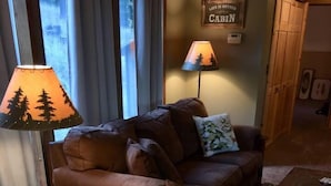A cozy living room with a brown leather couch, a table with a lamp, and a sign that reads "Life is better in Cabin."