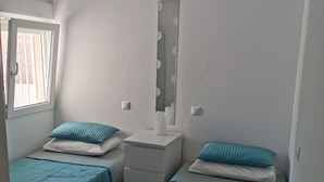 Una habitación pequeña y bien iluminada con dos camas individuales, una mesita de noche, un espejo y un ventilador de techo.