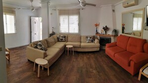 Una sala de estar con un sofá seccional color beige, un sofá rojo, una mesita de madera y una chimenea.