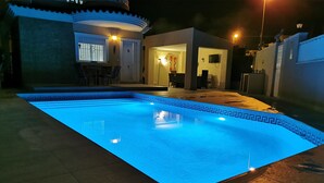 Una piscina con borde de azulejos, rodeada por un patio con sillas y una mesa.