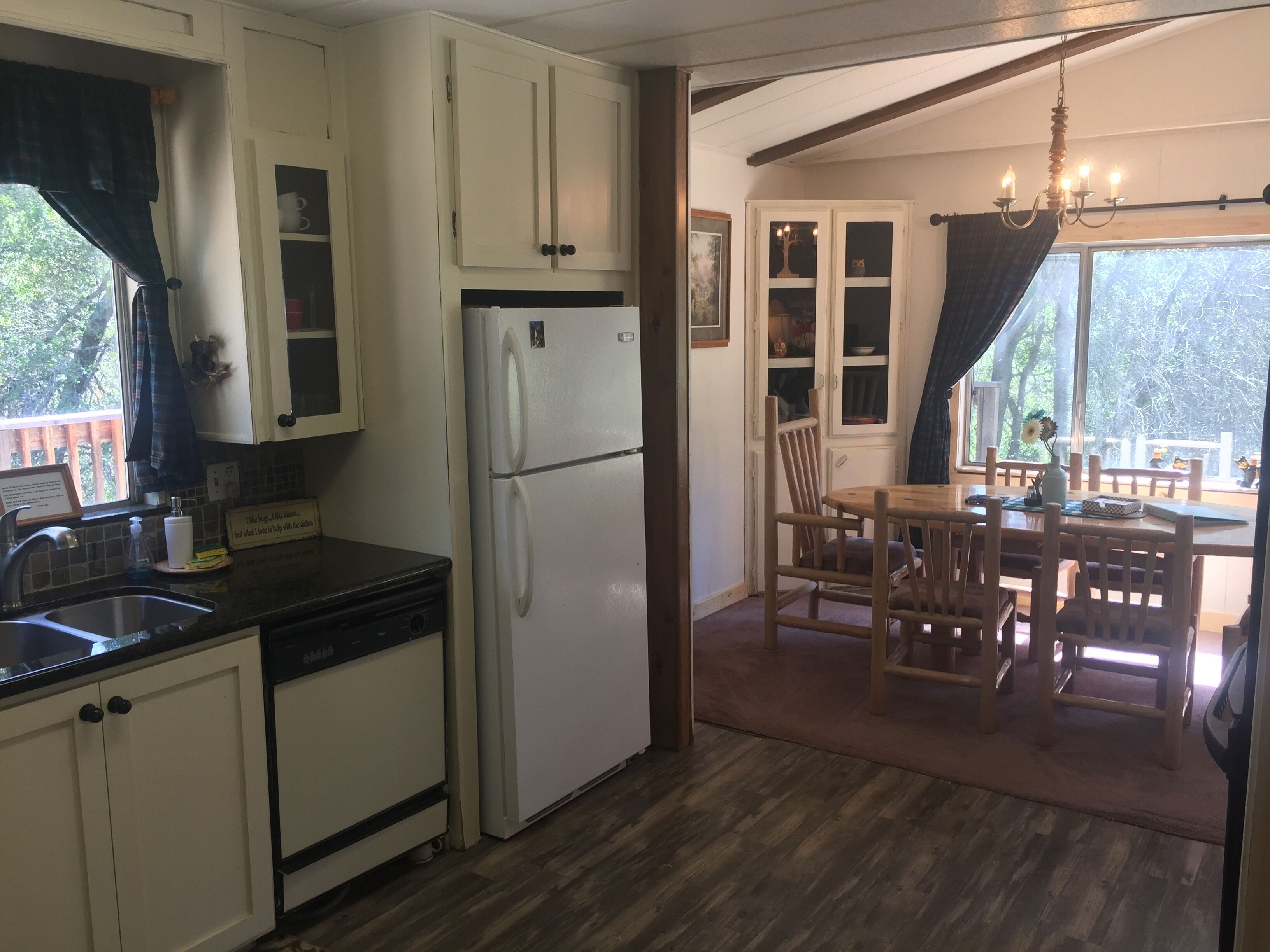 A kitchen with white cabinets, a refrigerator, a sink, and a dining area with wooden chairs and a table.
