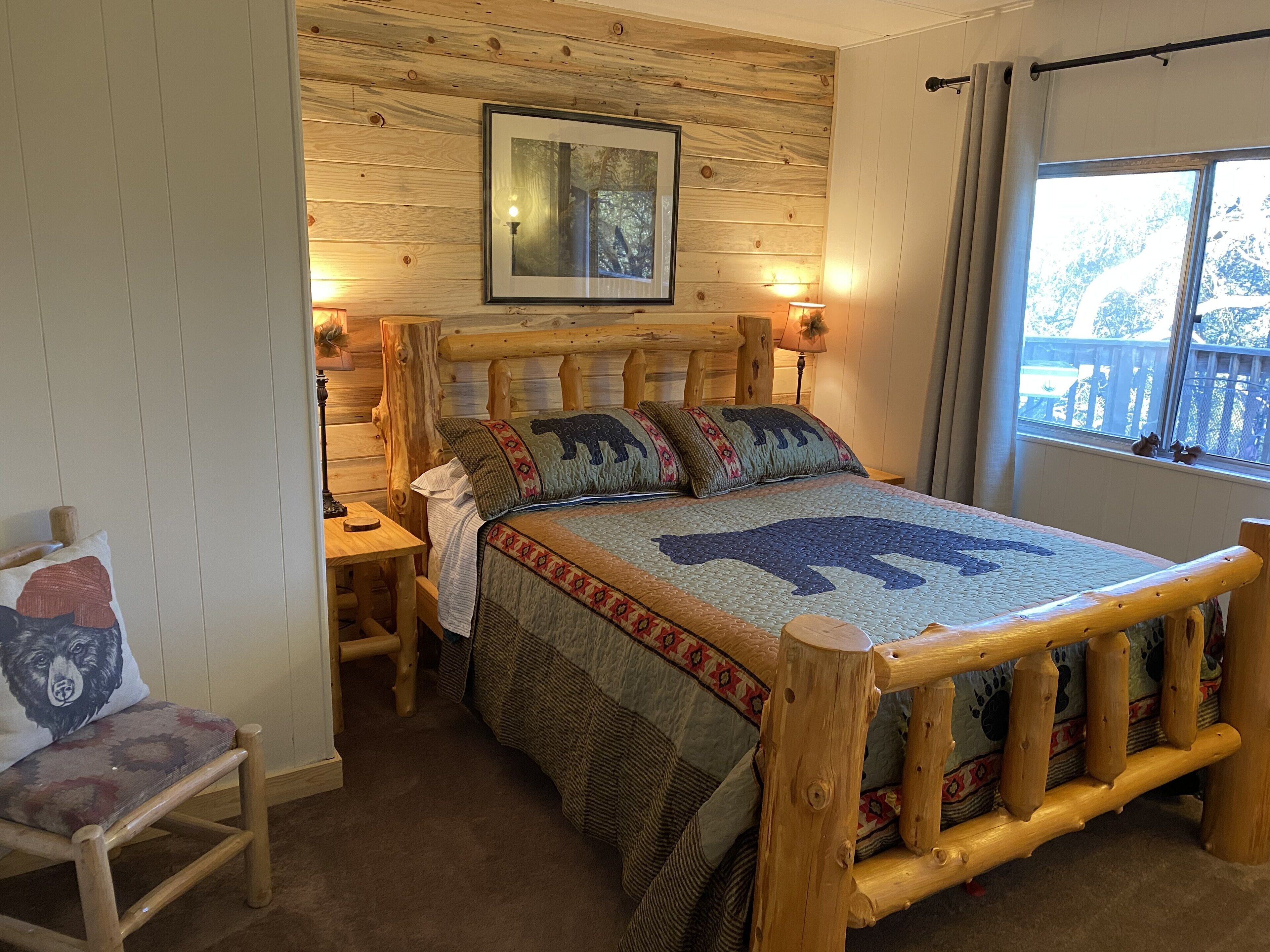 A wooden bed with a bear-themed quilt, a wooden headboard, and a window with a view of trees.