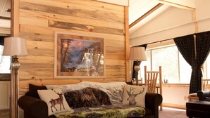 Quarto aconchegante com parede de madeira, pintura emoldurada, sofá com almofadas decorativas e janela com cortinas.
