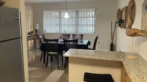 A compact kitchen with a refrigerator, dining table, chairs, and a window with blinds. - MINS from Everything -Private House 3/2- Pet Free/Smoke Free (Pembroke Pines)