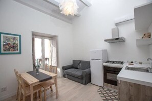 Cocina compacta con refrigerador, estufa y lavamanos. Hay una mesa de comedor con sillas y un sofá gris.