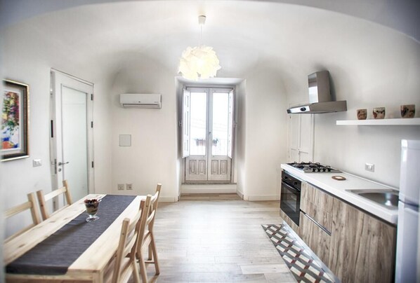 Cocina compacta con una isla central, zona de comedor con mesa y sillas, y un ventanal que proporciona luz natural.