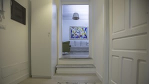 A hallway with a patterned rug, a framed abstract painting, and a green chair. - Residence Ventimiglia (Gangi)
