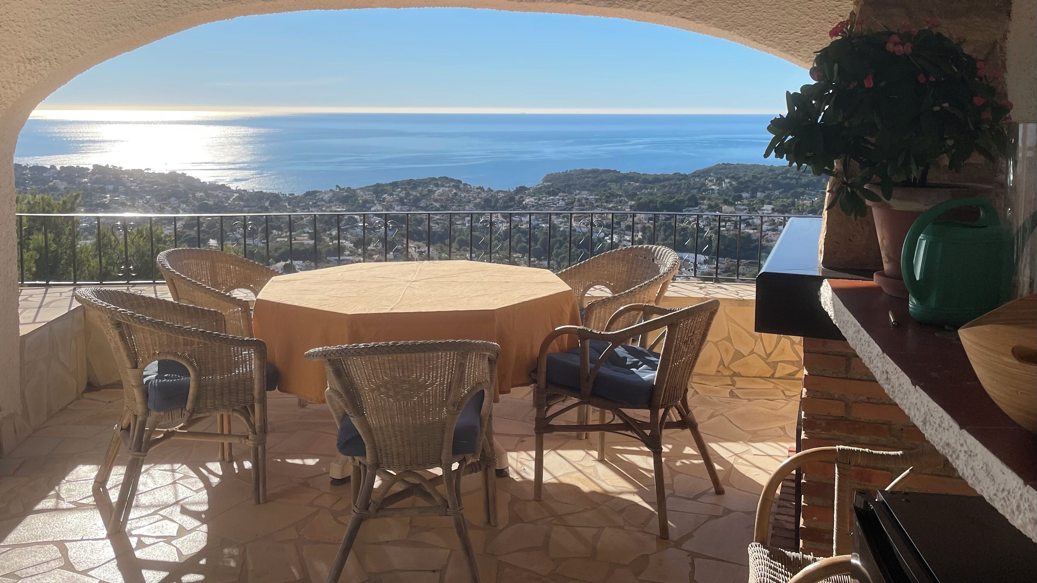 Una terraza con una mesa redonda y sillas de mimbre, con vistas a la costa.