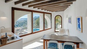 Une pièce dotée d’une grande fenêtre, d’un plafond en bois, d’une table à manger avec des chaises, et offrant une vue sur un paysage montagneux.