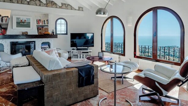 Un salon moderne doté d’une cheminée, d’un téléviseur et de grandes fenêtres en arc de cercle donnant sur la mer.
