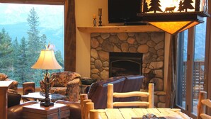 A cozy living room with a stone fireplace, comfortable seating, and a view of a forested mountain range. - Spectacular Views, Hiking & Skiing, Spacious Cozy Luxury, Hot tub, Fireplace (Breckenridge)
