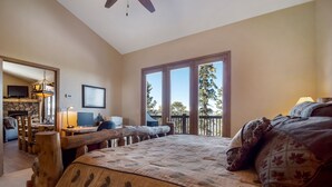 A bedroom with a large bed, a desk with a computer, a fireplace, and a balcony with a view of trees. - Spectacular Views, Hiking & Skiing, Spacious Cozy Luxury, Hot tub, Fireplace (Breckenridge)