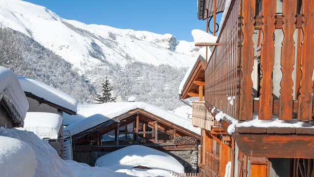 Un chalet en bois doté d’un balcon, entouré de montagnes enneigées.