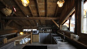 Une cuisine rustique avec des poutres en bois, un poêle, un évier et une fenêtre donnant sur un paysage agréable.