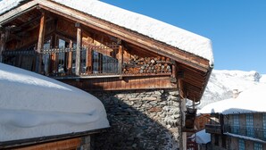 Un chalet en bois, doté de fondations en pierre, d’un toit enneigé et d’un balcon avec des balustrades en bois.