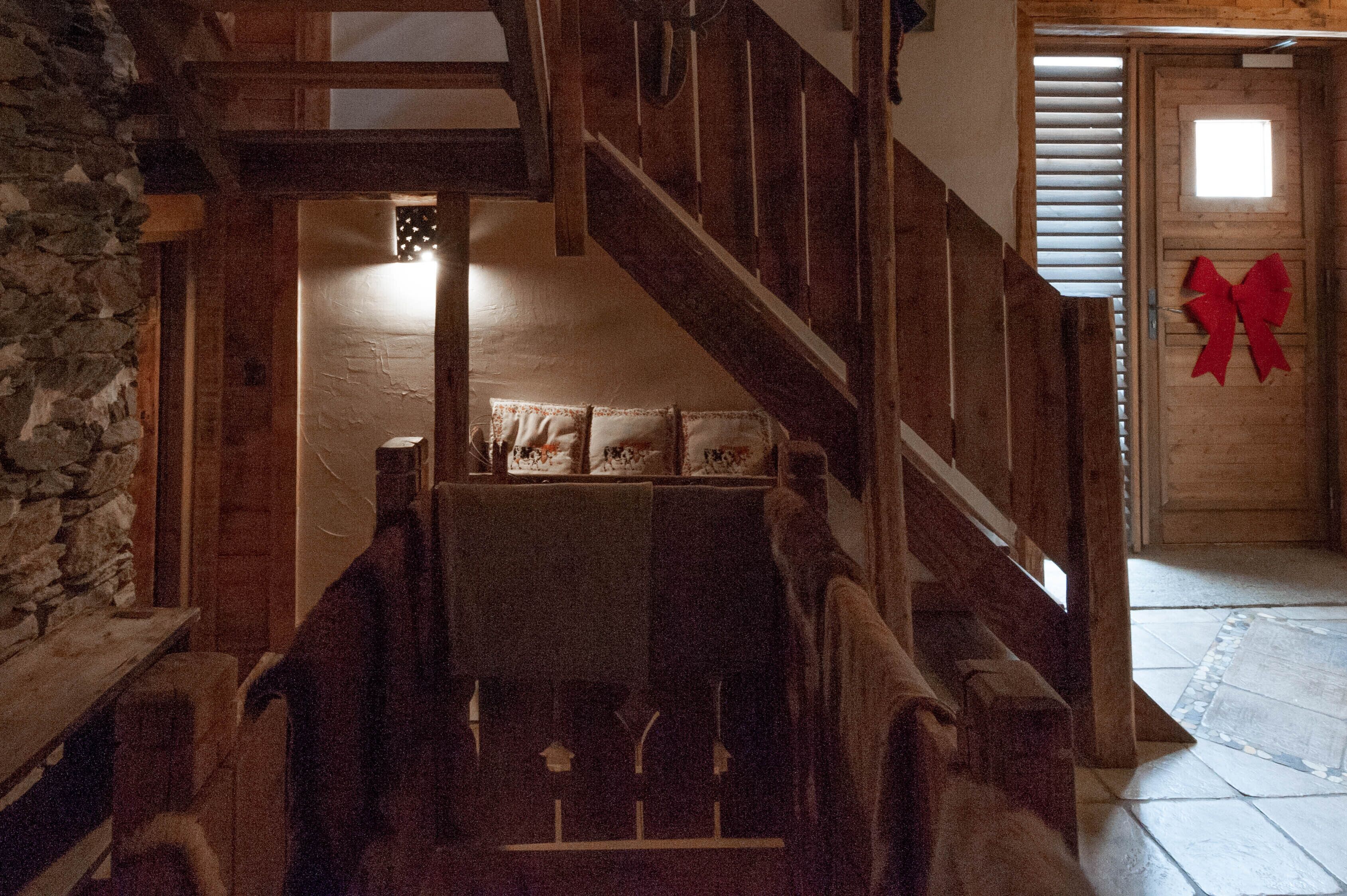 A wooden staircase leading to a room with a stone wall and a red bow decoration on the door.