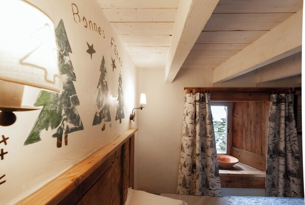 A narrow hallway with wooden walls and a wooden bench. There is a wall with Christmas decorations and a window with curtains.